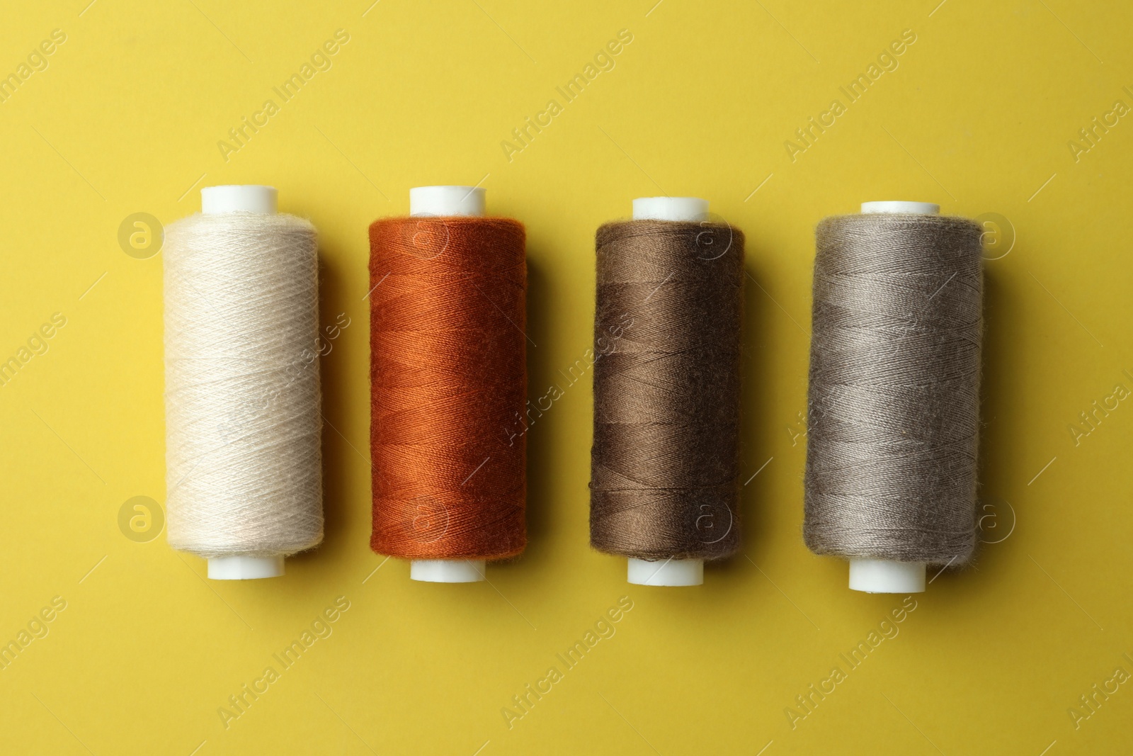 Photo of Different colorful sewing threads on yellow background, flat lay