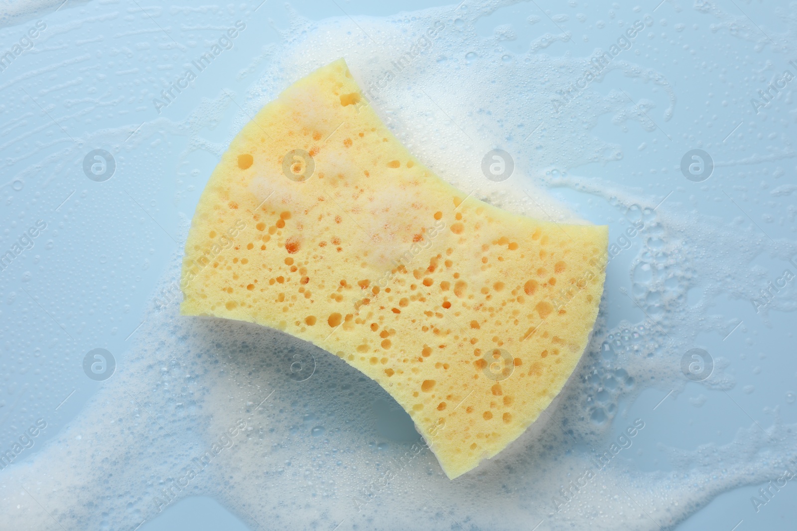 Photo of Yellow sponge with foam on light blue background, top view