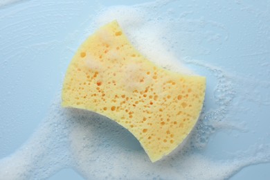 Photo of Yellow sponge with foam on light blue background, top view