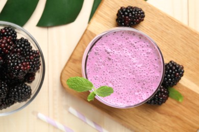 Photo of Delicious blackberry smoothie in glass and berries on wooden table, flat lay