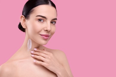 Photo of Beautiful woman with smear of body cream on her neck against pink background, space for text