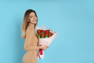 Photo of Happy woman with red tulip bouquet on light blue background, space for text. 8th of March celebration