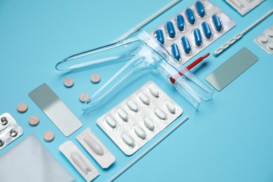 Photo of Sterile gynecological examination kit and pills on light blue background