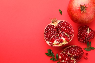 Fresh pomegranates and green leaves on red background, flat lay. Space for text