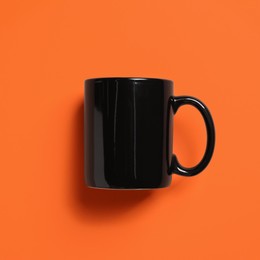 Photo of One black ceramic mug on orange background, top view