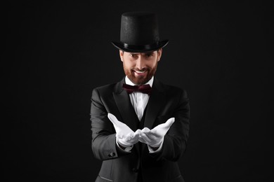 Happy magician in top hat on black background