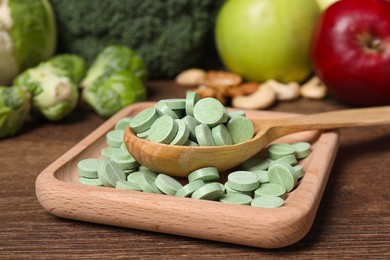 Photo of Spoon with pills and foodstuff on wooden table, closeup. Prebiotic supplements