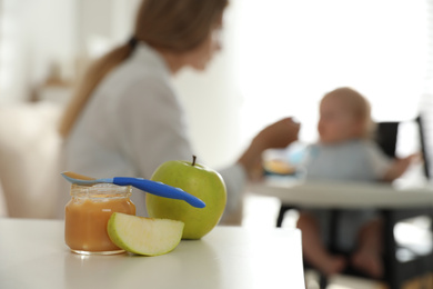 Mother feeding her little baby at home, focus on healthy fruit puree and fresh apples