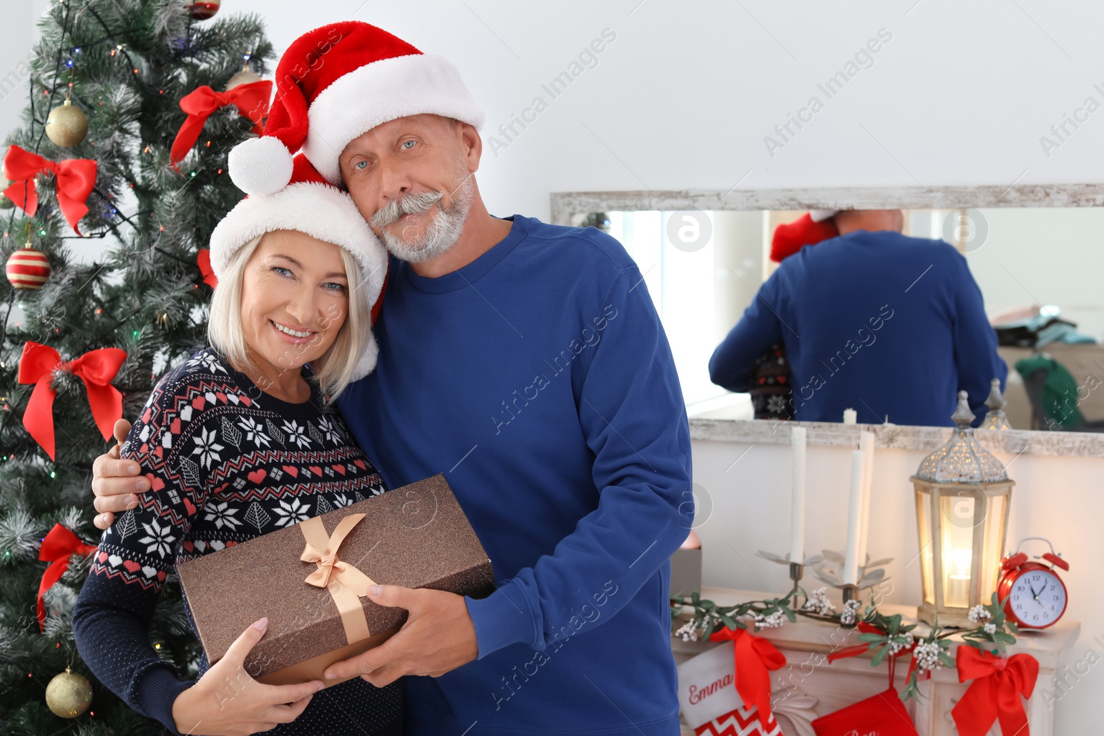 Photo of Mature couple in Santa hats with Christmas gift box at home