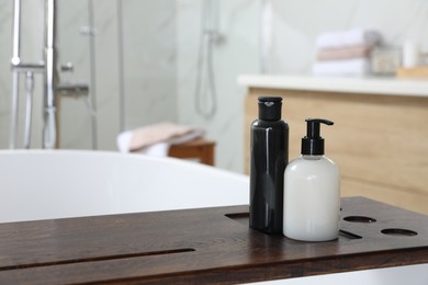 Wooden bath tray with bottles of shower gels on tub indoors, space for text