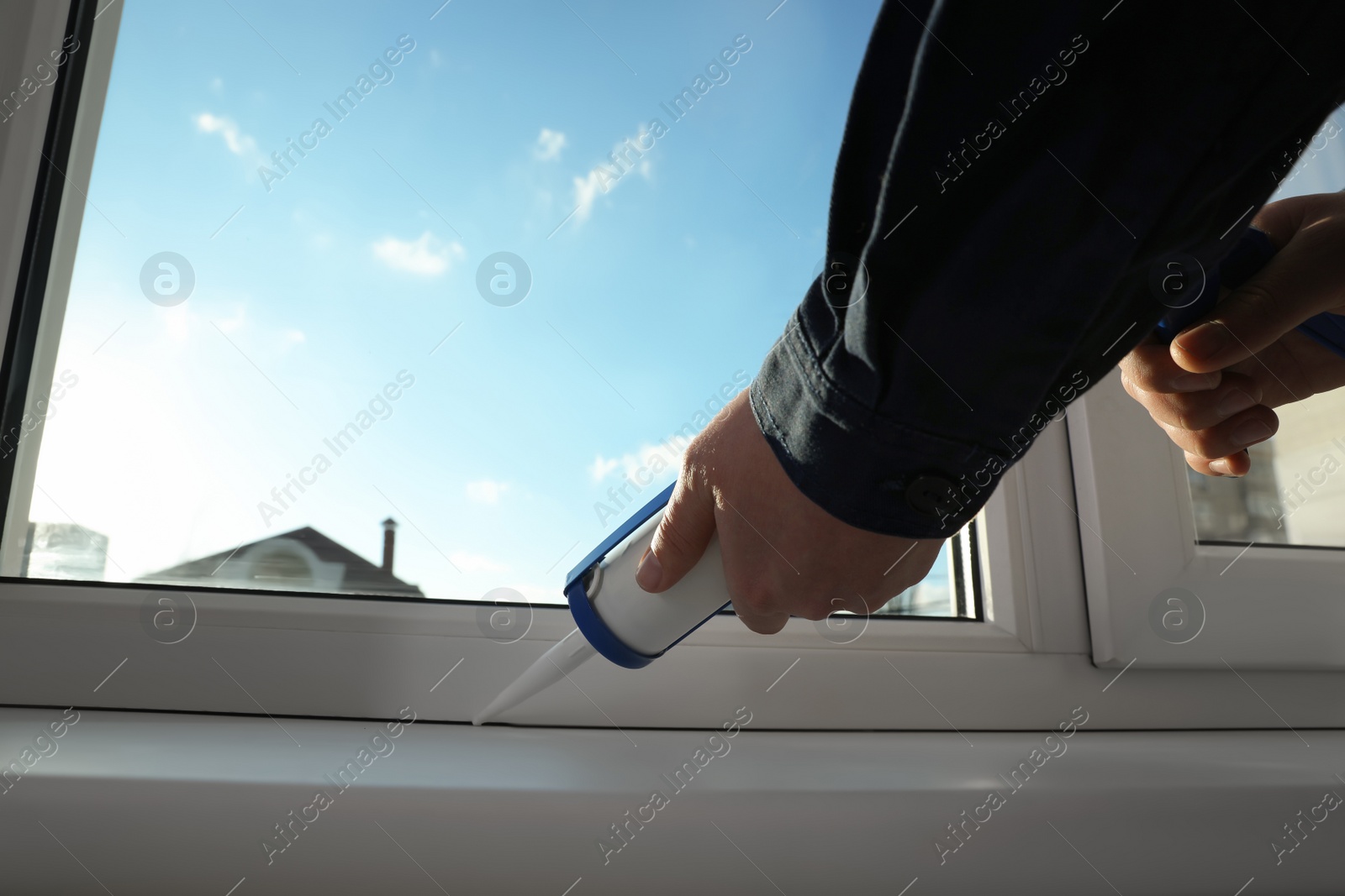 Photo of Construction worker sealing window with caulk indoors, closeup