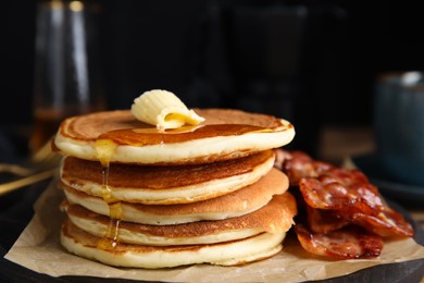 Delicious pancakes with maple syrup, butter and fried bacon on wooden board, closeup