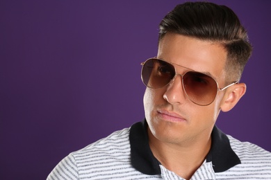 Photo of Handsome man wearing sunglasses on purple background, closeup. Space for text