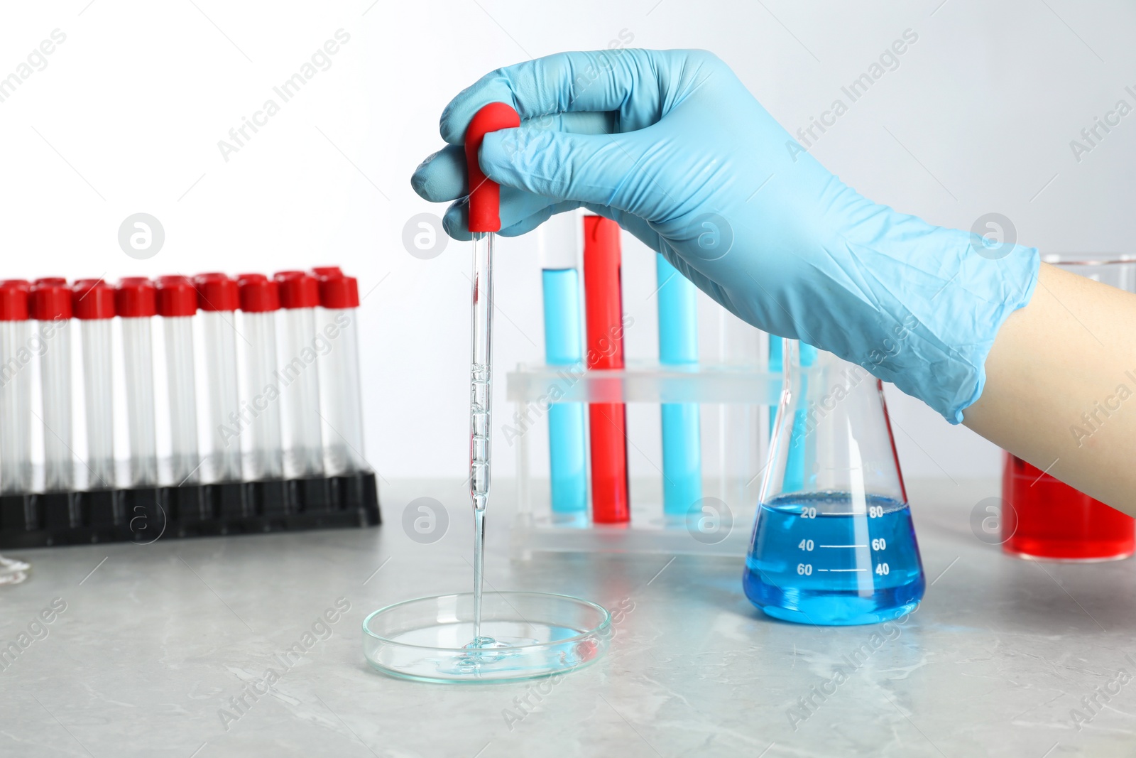 Photo of Scientist dripping liquid from pipette into petri dish at grey marble table, closeup