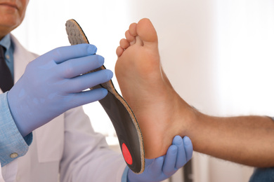 Male orthopedist fitting insole on patient's foot in clinic, closeup