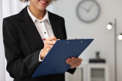 Photo of Notary with clipboard writing notes in office, closeup