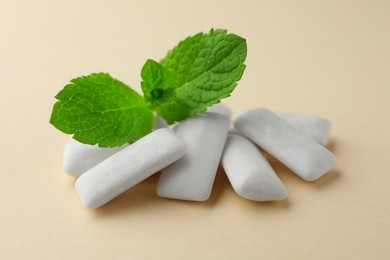 Tasty white chewing gums and mint leaves on beige background, closeup