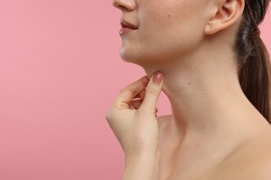 Woman touching her neck on pink background, closeup. Space for text