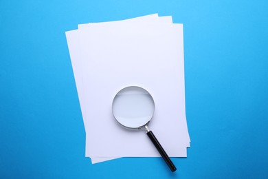 Photo of Magnifying glass and paper sheets on light blue background, top view