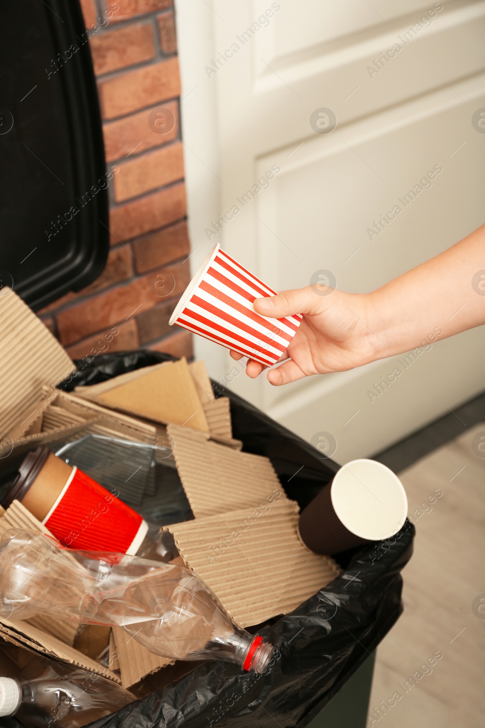 Photo of Young woman throwing popcorn cup in trash bin indoors, closeup. Waste recycling