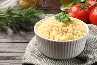 Delicious bulgur with parsley in bowl on wooden table, closeup