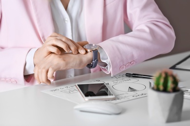 Young woman checking time on her wristwatch at workplace