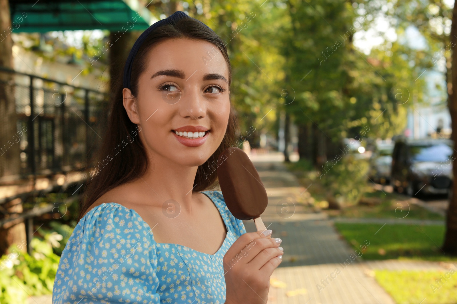 Photo of Beautiful young woman holding ice cream glazed in chocolate on city street