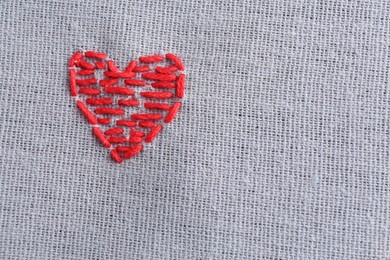 Embroidered red heart on gray cloth, top view. Space for text