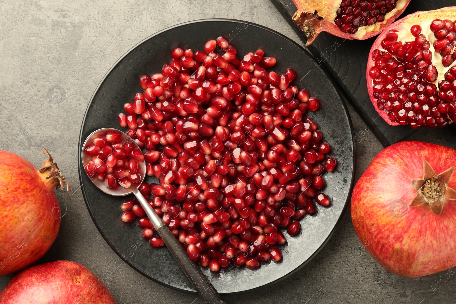 Photo of Ripe juicy pomegranates with grains on grey textured table, flat lay