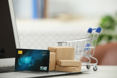 Online payment concept. Small shopping cart with bank card, boxes and laptop on table