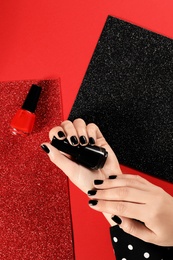 Woman with black manicure and nail polish bottles on color background, top view. Space for text
