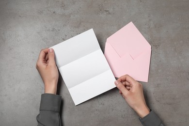 Photo of Woman with blank sheet of paper at grey textured table, top view. Space for text