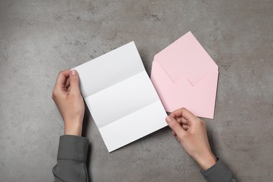 Woman with blank sheet of paper at grey textured table, top view. Space for text