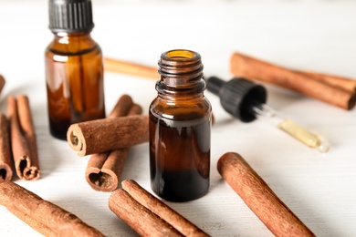 Photo of Bottles of essential oils and cinnamon sticks on white wooden table