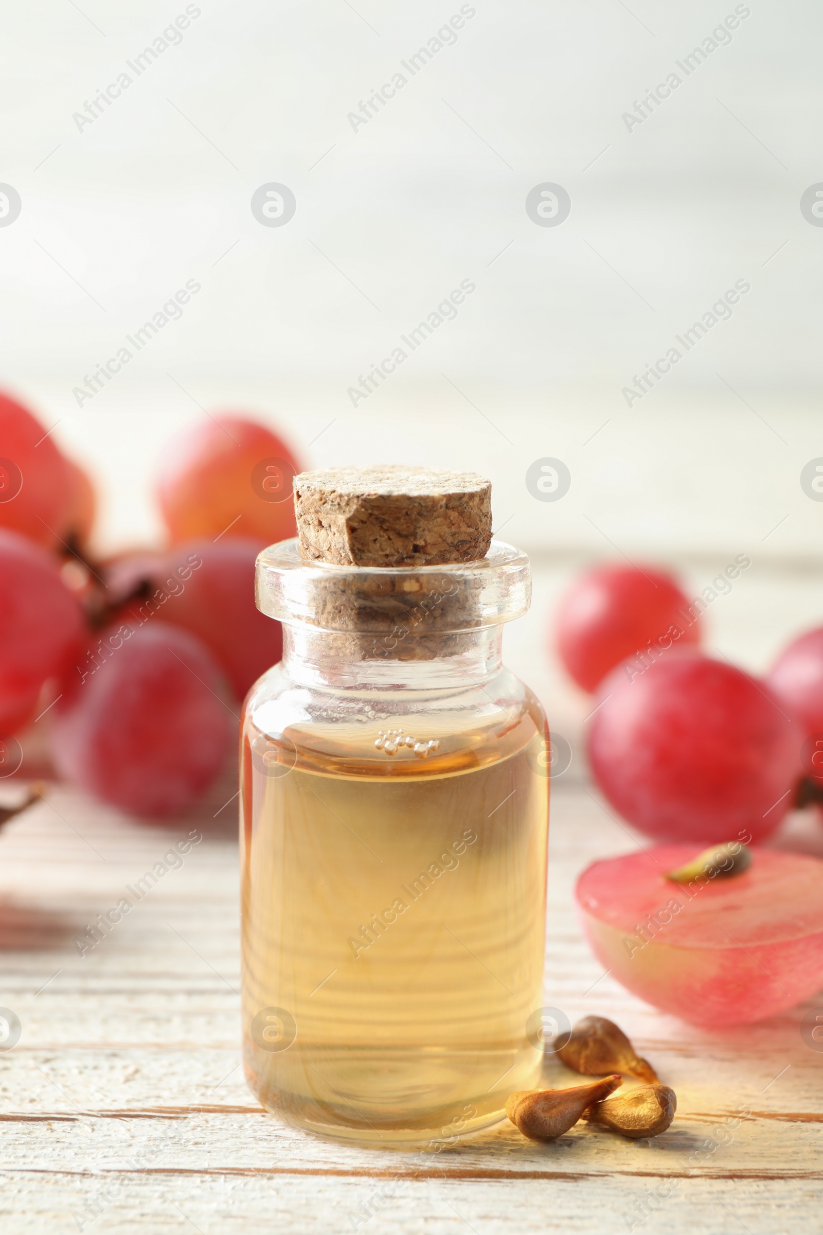 Photo of Organic red grapes, seeds and bottle of natural essential oil on white wooden table