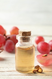 Organic red grapes, seeds and bottle of natural essential oil on white wooden table