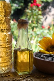 Bottles of sunflower oil and seeds on wooden table outdoors