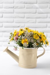 Photo of Beautiful bouquet of bright wildflowers in watering can on white wooden table near brick wall