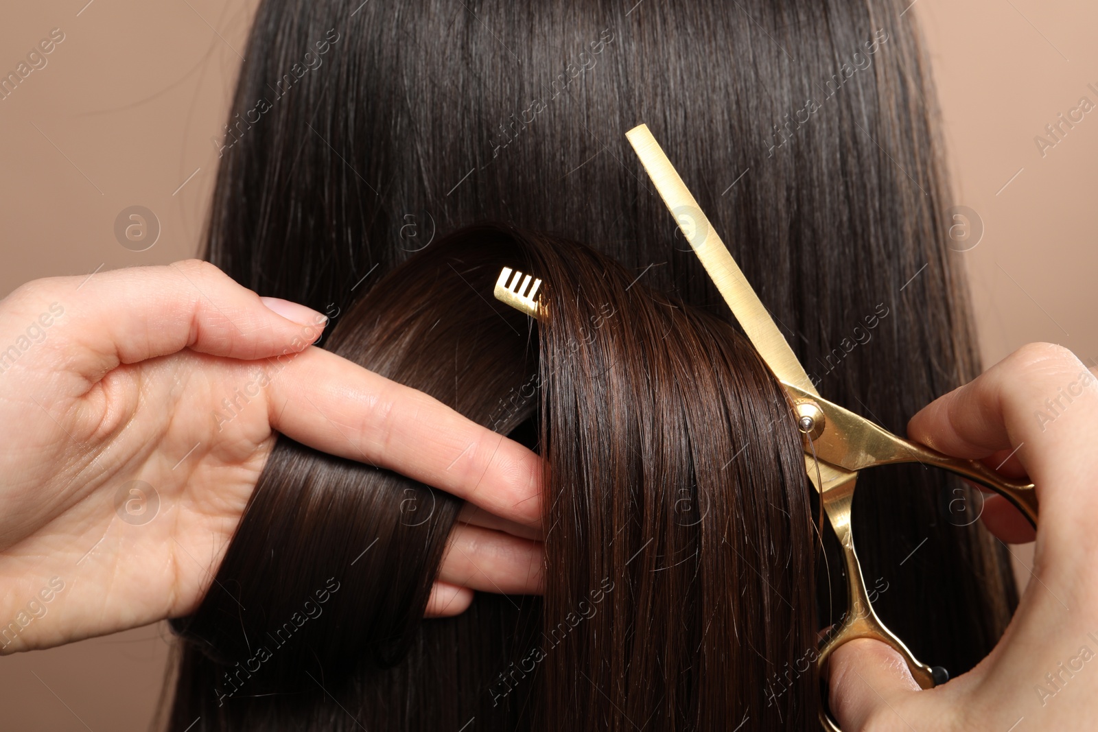 Photo of Hairdresser cutting client's hair with scissors on beige background, closeup