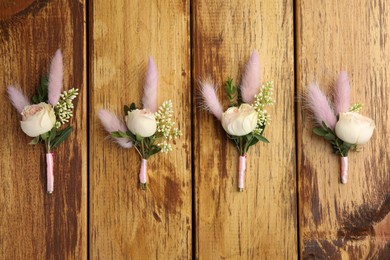 Many stylish boutonnieres on wooden table, flat lay