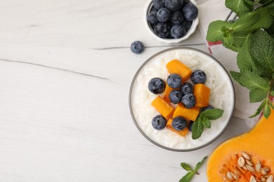 Photo of Bowl of delicious rice porridge with blueberries, pumpkin and mint on white table, flat lay. Space for text