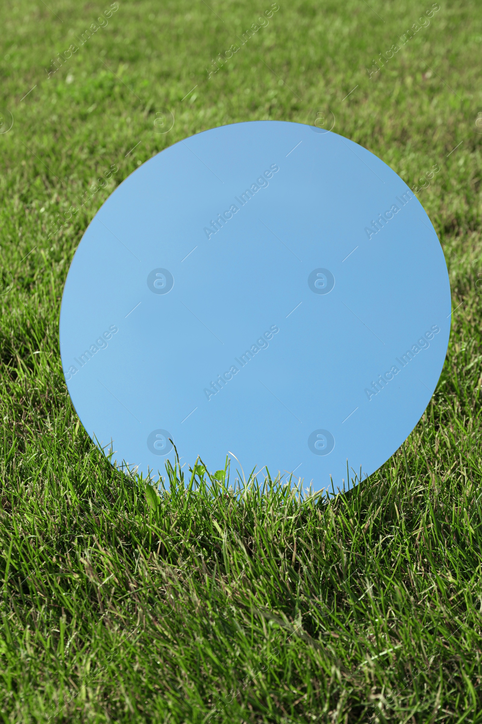 Photo of Round mirror on grass reflecting sky on sunny day