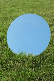 Round mirror on grass reflecting sky on sunny day