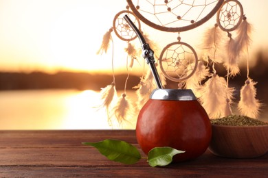 Image of Calabash with mate tea and bombilla on wooden table outdoors at sunset. Space for text