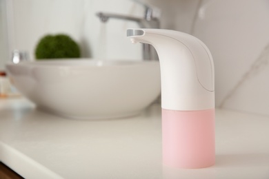 Photo of Modern automatic soap dispenser on countertop in bathroom. Space for text