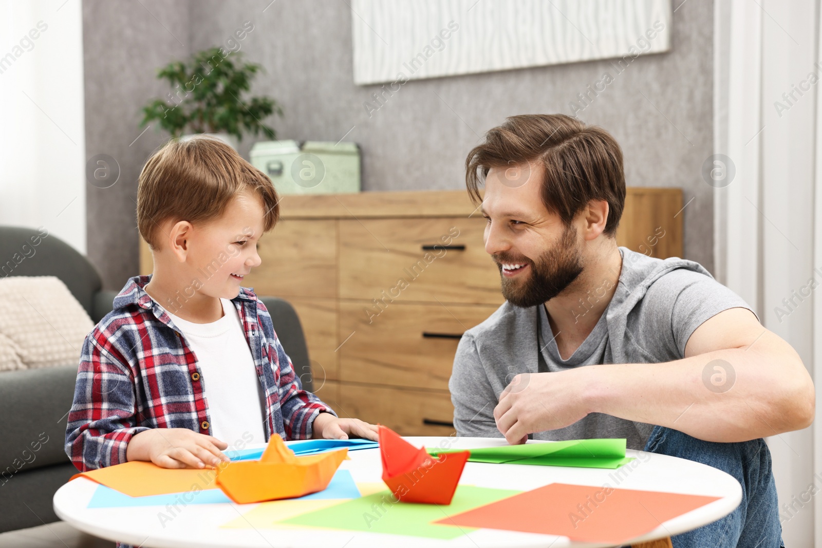 Photo of Dad and son making paper boats at coffee table indoors