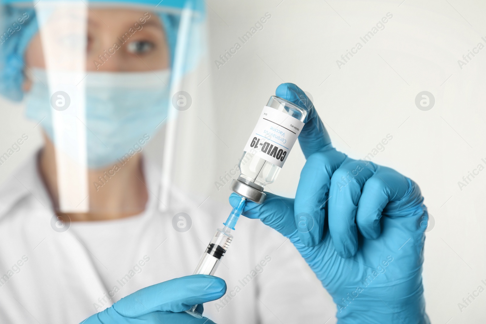 Photo of Doctor filling syringe with Covid-19 vaccine against white background, focus on hands