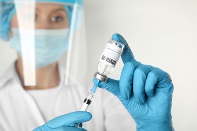 Doctor filling syringe with Covid-19 vaccine against white background, focus on hands