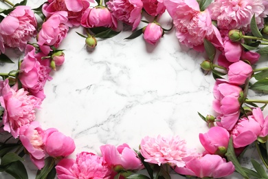 Frame made of fragrant peonies on marble table, top view with space for text. Beautiful spring flowers