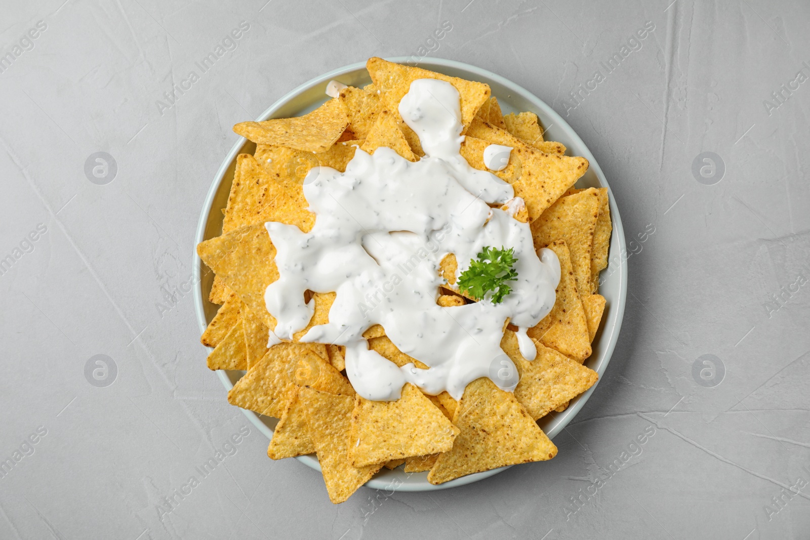 Photo of Plate of Mexican nacho chips with sauce on grey table, top view